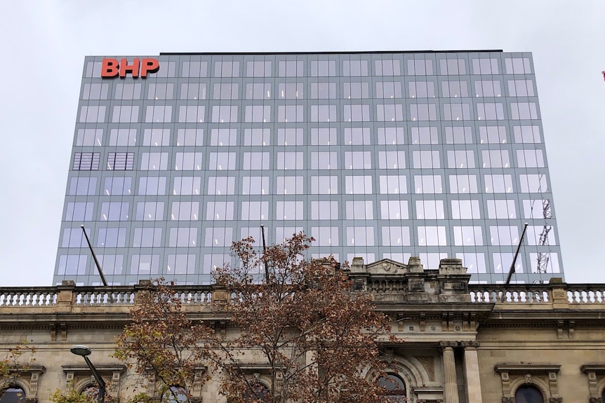 A large modern rectangular building with a BHP logo on it behind a 19th century stone building