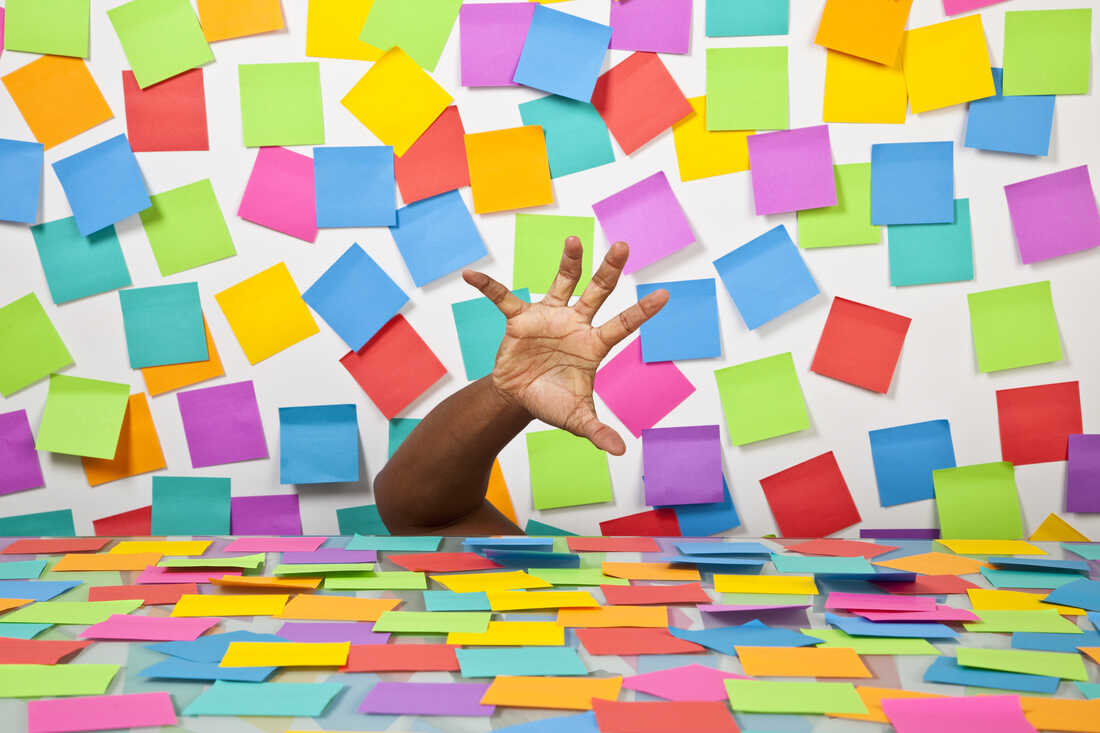 Hand reaching up over a desk covered in colorful post-it notes, representing the completely overwhelming feeling of starting a new job.