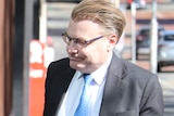 A close shot of WA Ombudsman Chris Field walking into a building wearing spectacles, a dark grey suit, blue tie and white shirt.